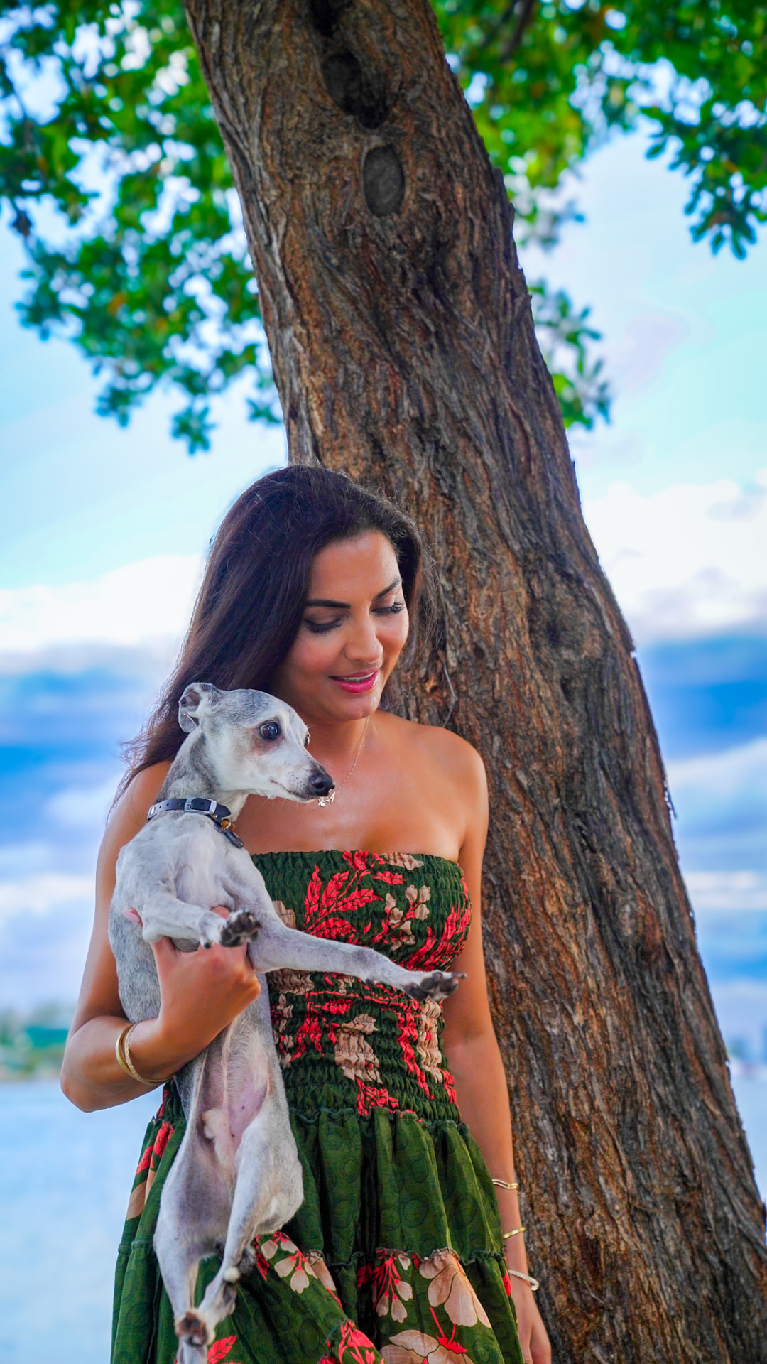 Elmira holding one of her greyhounds beneath a sea grape tree