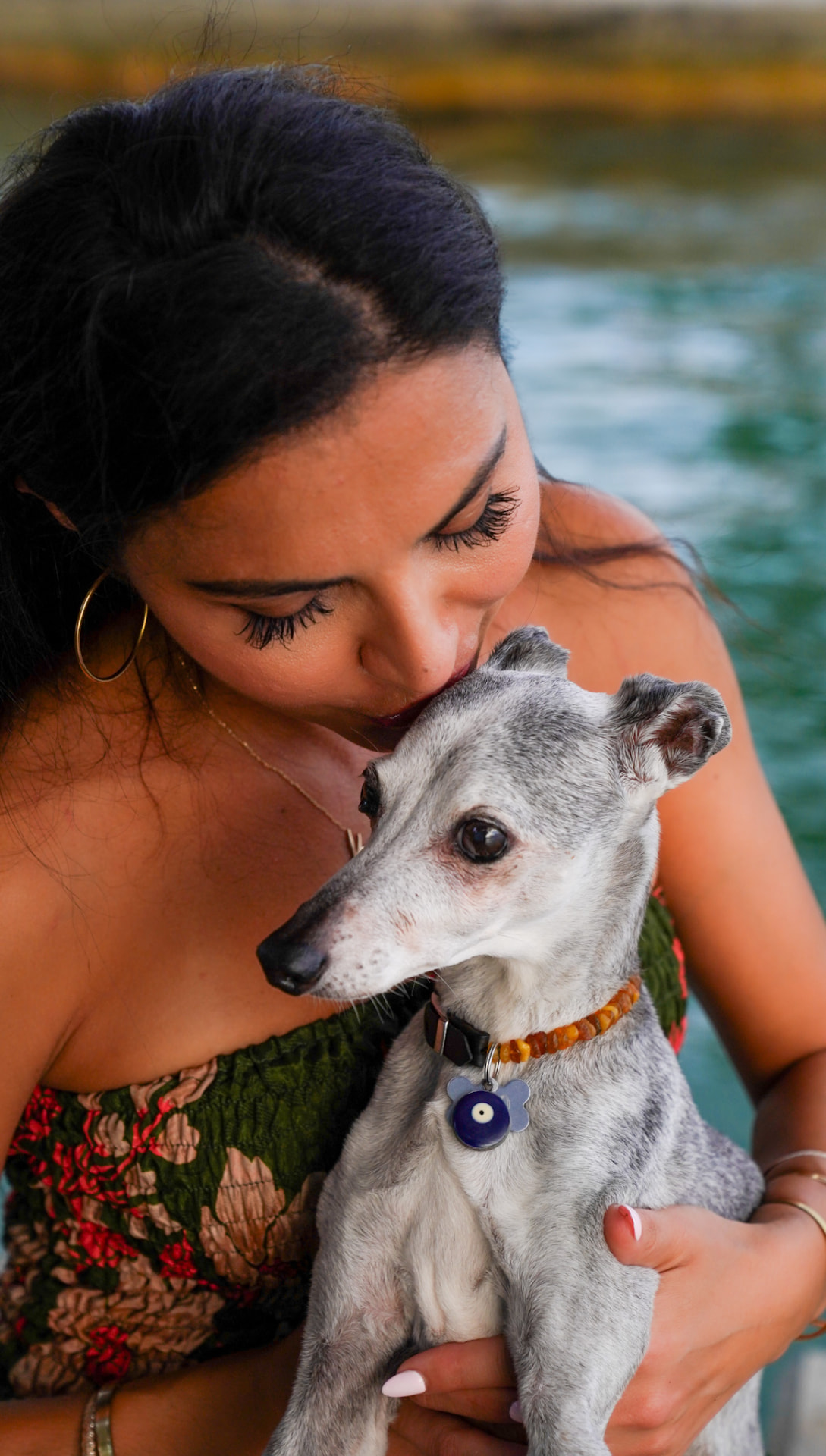 Elmira resting her face against one of her greyhounds by the water