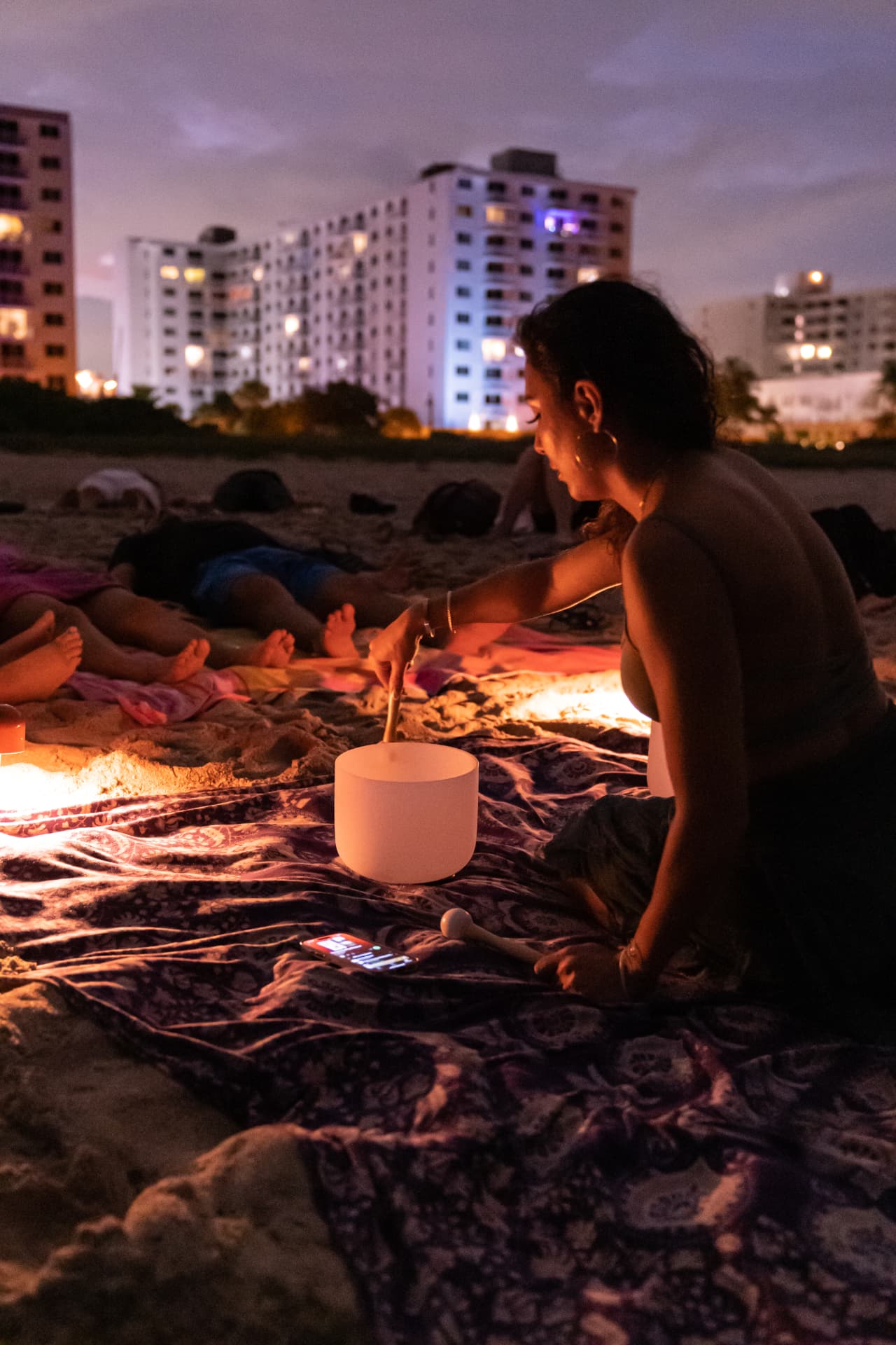 Guests lying back on the sand while Elmira plays a crystal bowl at dusk