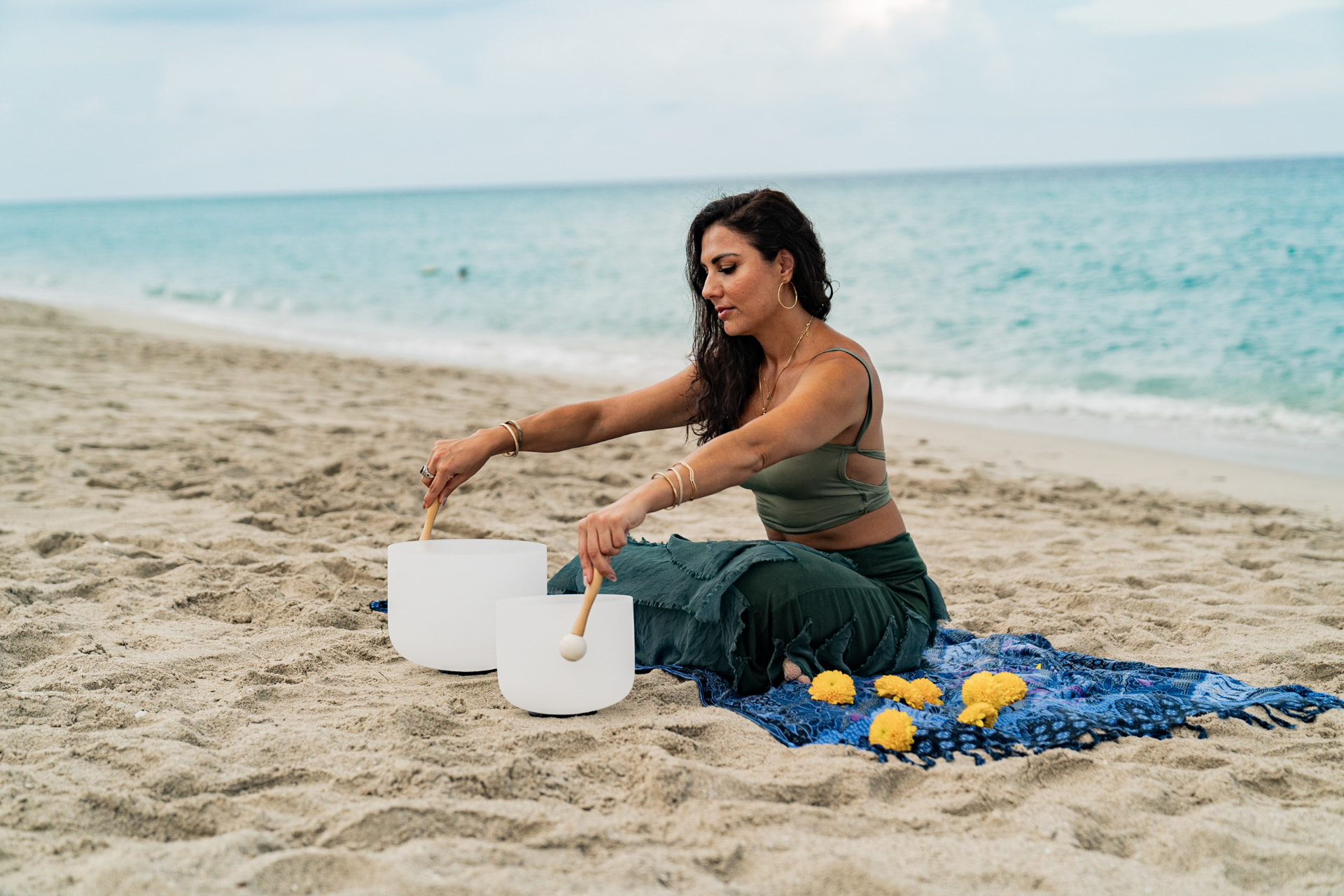 Elmira playing two crystal bowls on the sand beside the ocean