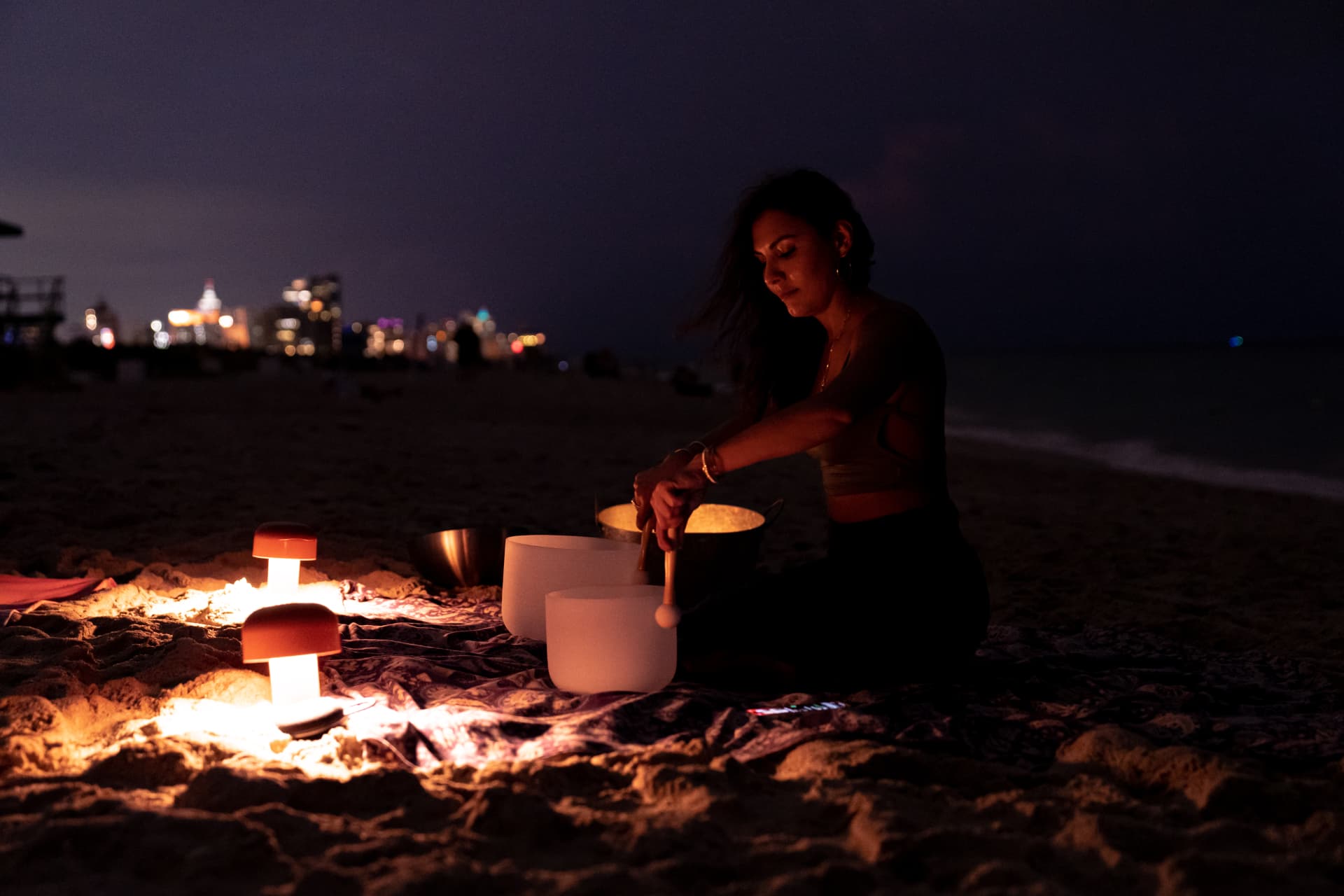 Elmira playing crystal bowls by lantern light on the sand after dark